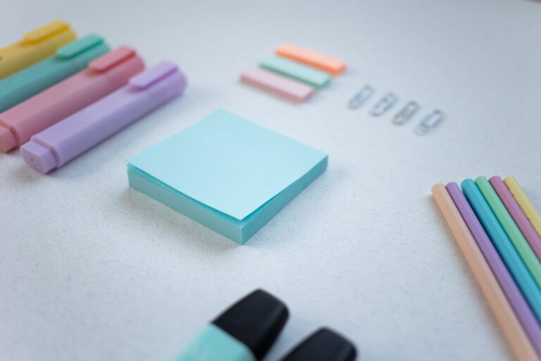 Flat lay of pastel stationery items including highlighters, sticky notes, and paper clips on a white surface.
