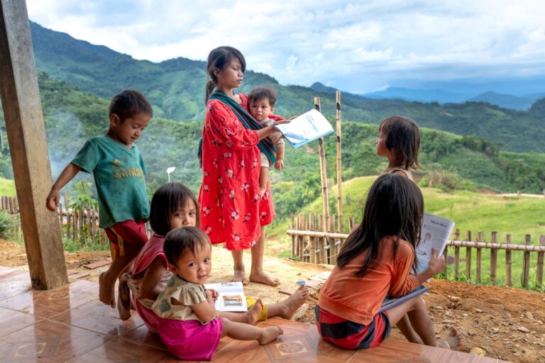 Young children reading books in a rural mountain village, embracing education amidst nature.
